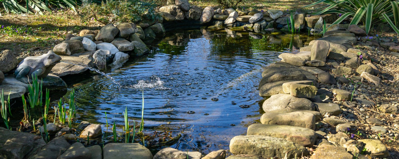 Gartenteich gestalten mit natürlichen Teichsteinen und Kies für den Teich – harmonische Teichumrandung aus Basalt und Granit, klares Wasser mit Wasserpflanzen.